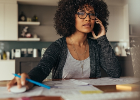 a black woman sits in her home office holding a cell phone to her ear