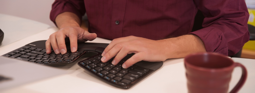 a man sits at a desk typing on a ergonomic keyboard with a separation in the center