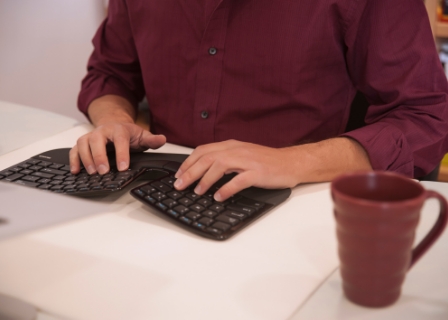 a man is at a desk typing on a ergonomic keyboard that has a separation in the center
