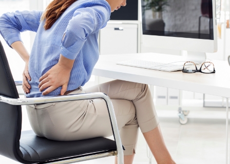 a woman at her desk holding her lumbar in pain