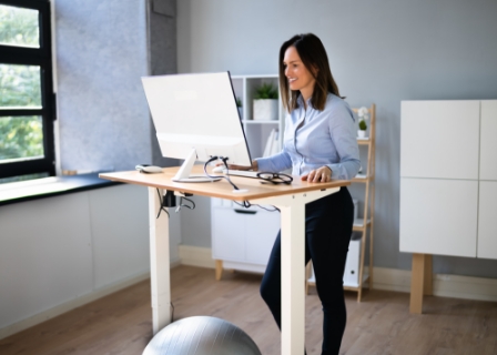 a woman stands at an adjustable height desk in her home office smiling