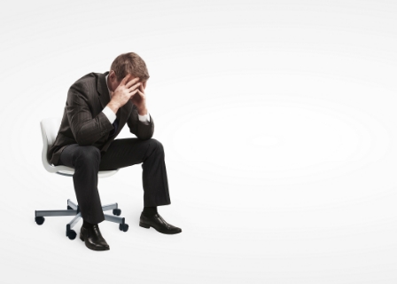 a man in a suit sits in an office chair clutching his head