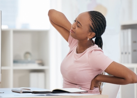 a black woman in a home office clutches her back in two different places