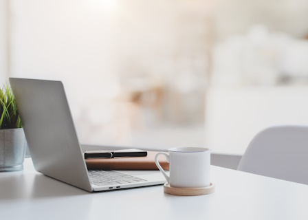 a desk with a plant a mug and an open laptop